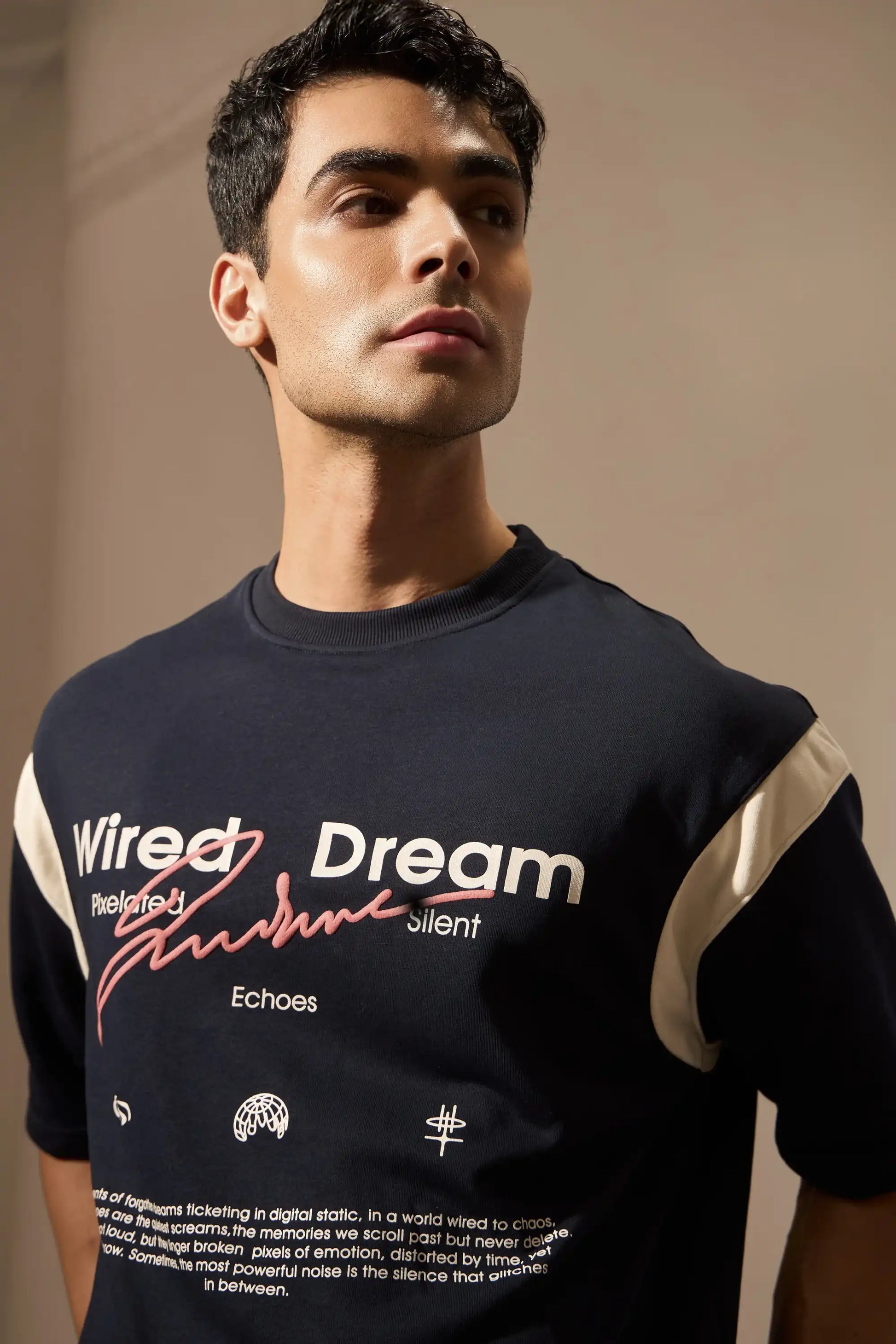 Man wearing a navy t-shirt with text and graphics on a beige background