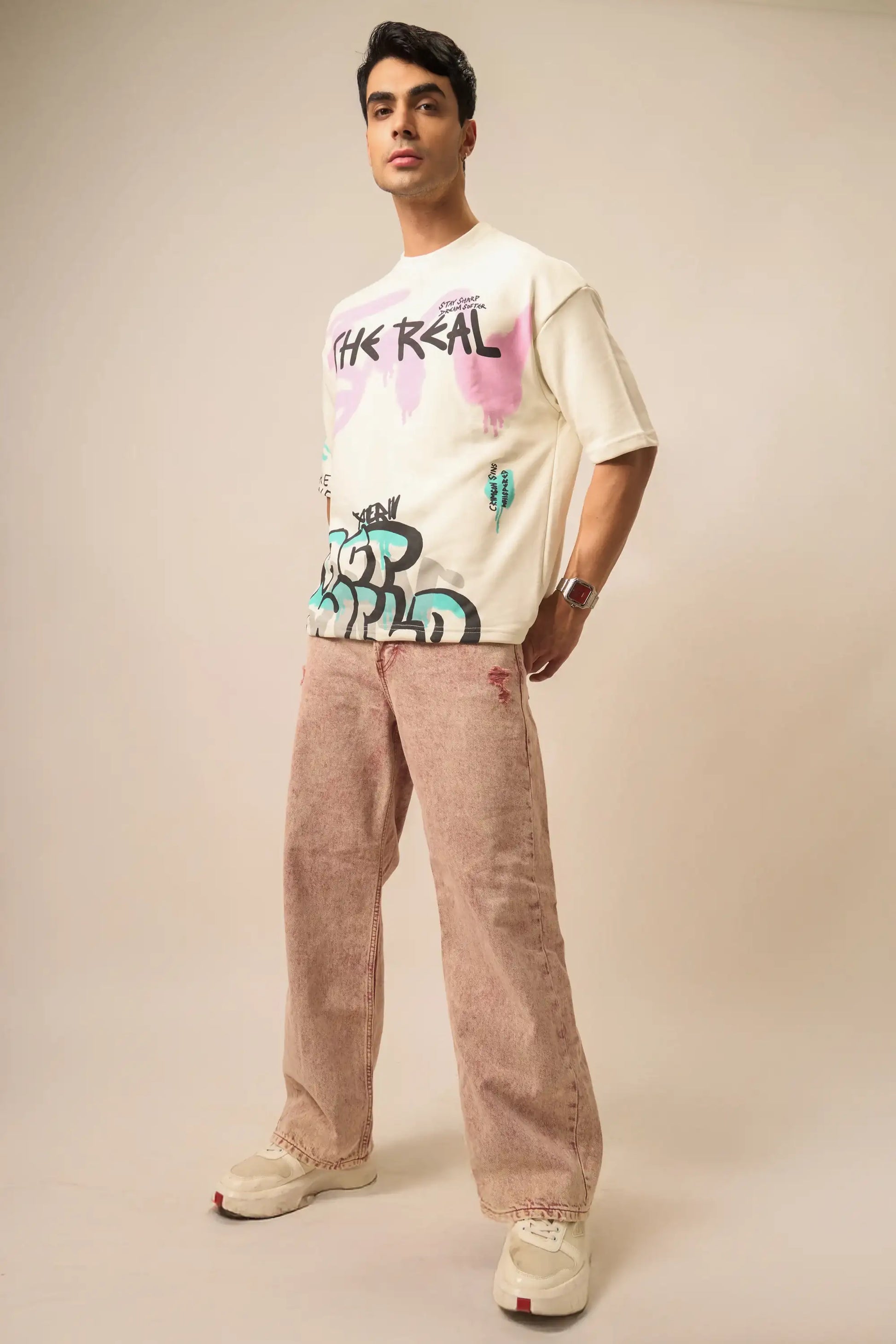 Man wearing a graphic t-shirt and beige pants on a plain background