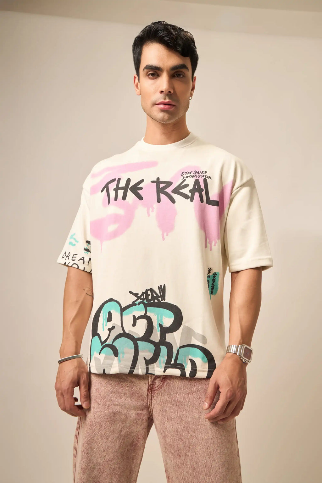 Man wearing a cream t-shirt with colorful graffiti design and graphics on a plain background